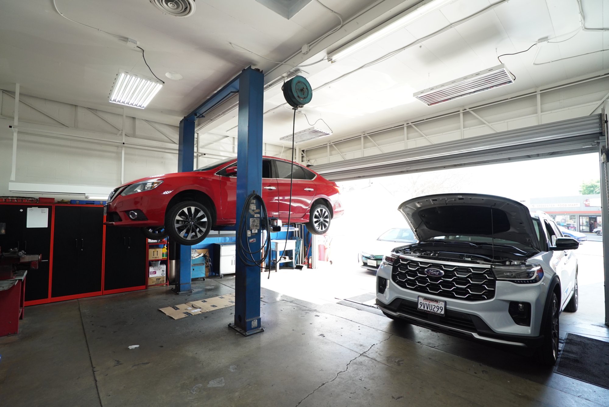 Active service bays at Sam's Auto Repair — red Nissan on lift and Ford SUV with hood open Eagle Rock